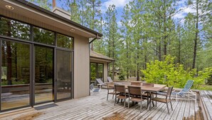 Um deck de madeira com uma mesa e cadeiras de jantar, com vista para uma área arborizada.