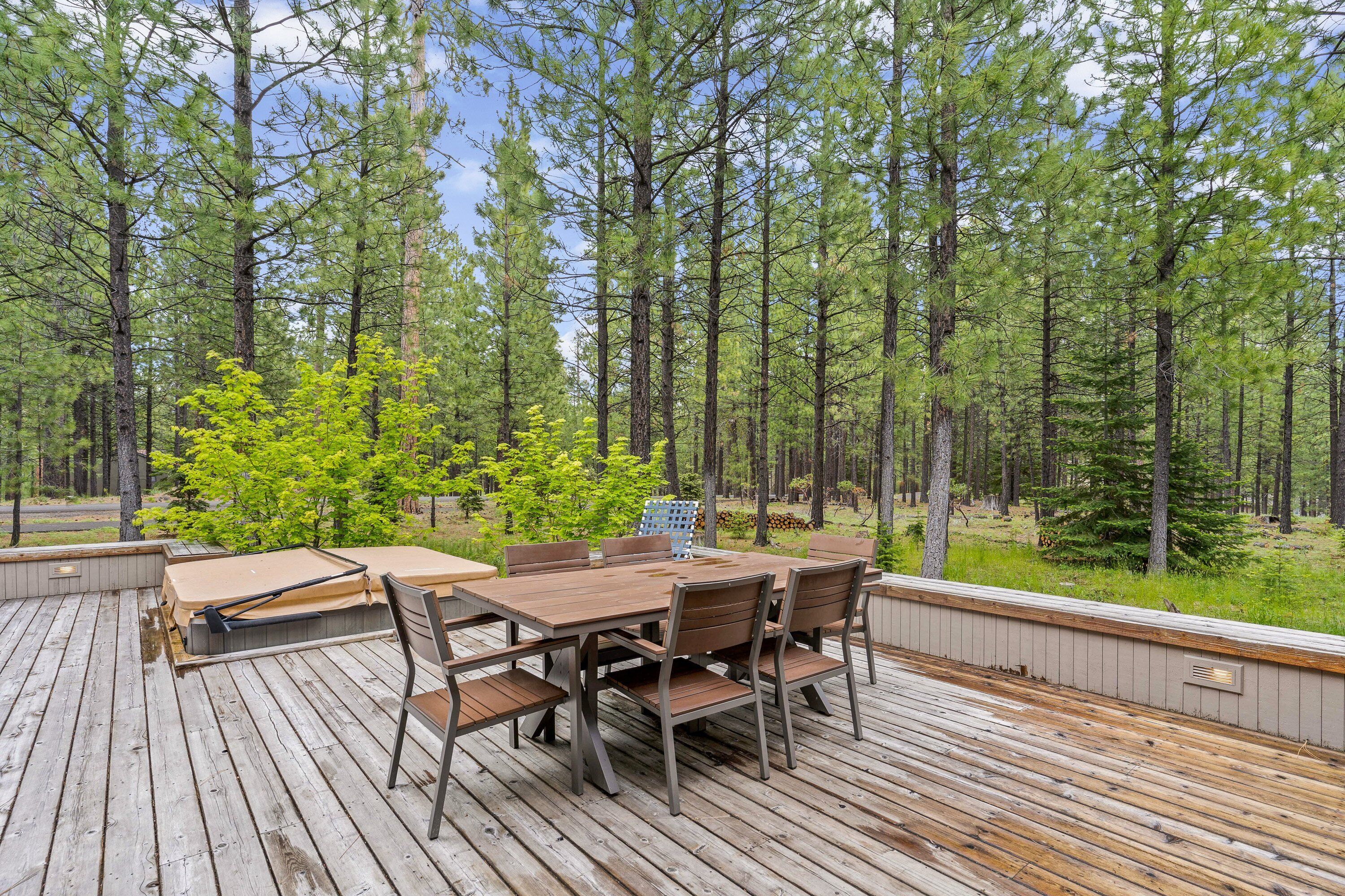 Een terras buiten met een houten tafel en stoelen, omgeven door hoge dennenbomen.