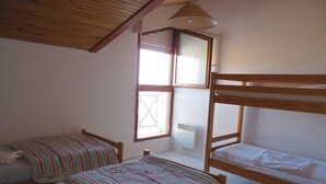 A room with two bunk beds, a window with blinds, a radiator, and a ceiling fan.