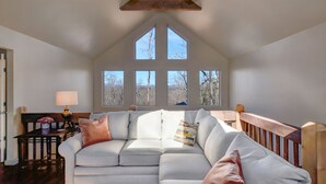 Un salon spacieux, doté d’un grand canapé d’angle, d’un plafond en bois et de nombreuses fenêtres offrant une vue sur l’extérieur.