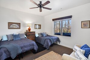 A bedroom with two beds, a ceiling fan, a window with a view of trees, and a dresser with a lamp. - Spacious Luxury 3 Level Cabin w Hot Tub & Fire Pit  (Blue Ridge)