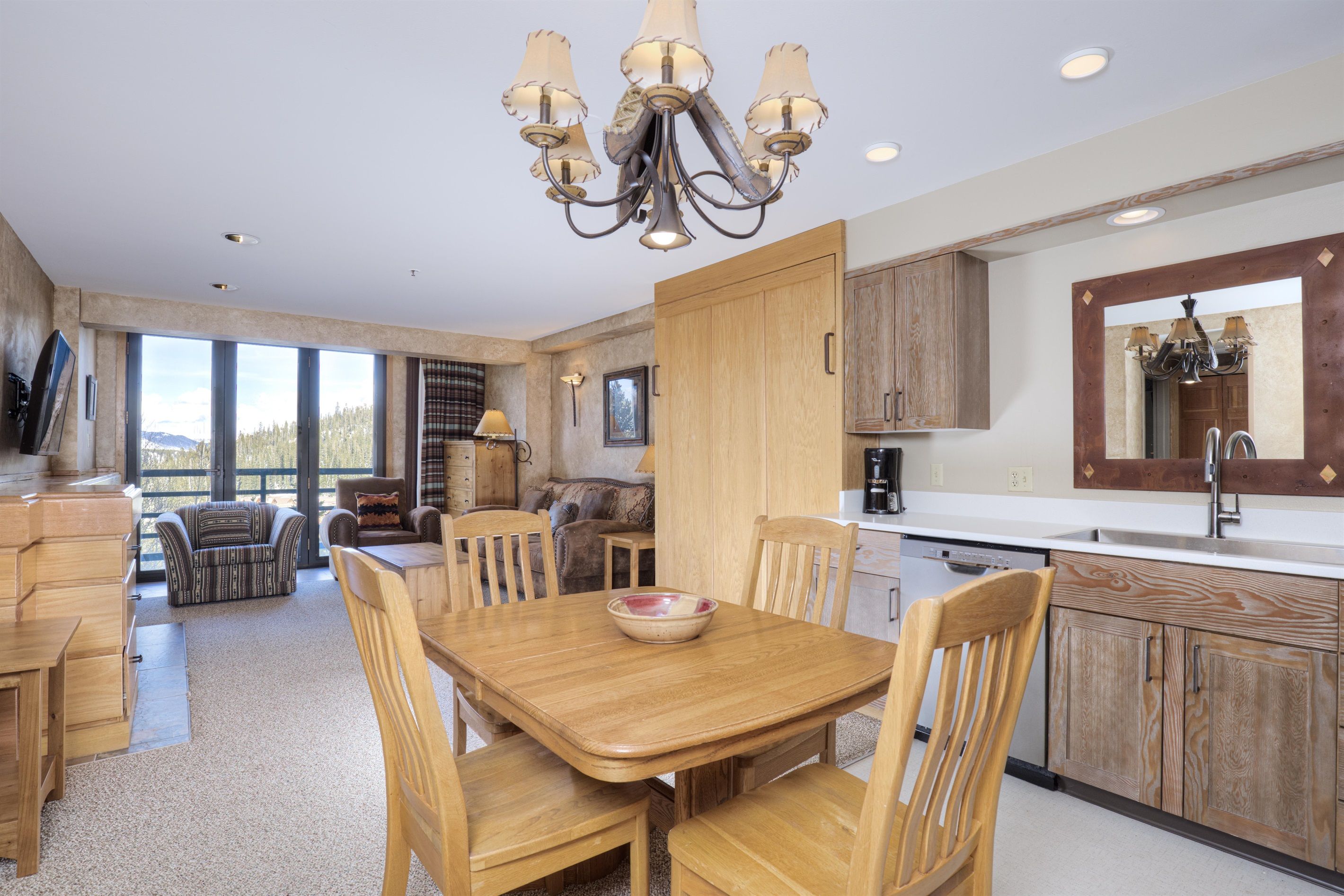 A modern kitchen with wooden cabinets, a dining table with chairs, and a large window offering a view of the outdoors.