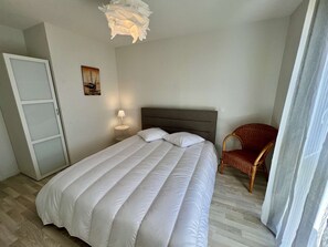Une chambre à coucher avec un lit, une table de chevet, une lampe, une chaise et une porte.