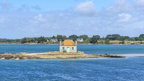 A small stone house with a blue door and windows on a rocky shoreline by a large body of water. - Etel - 2-room apartment - 43 sqm - Wifi - Classified 3* (ETEL)