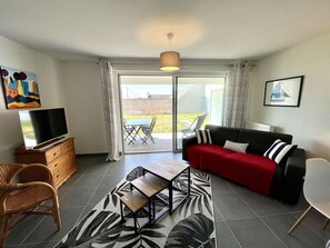 Un salon moderne comprenant un canapé, un téléviseur et un coin repas avec des chaises et une table.
