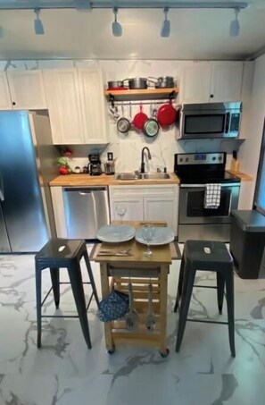 A compact kitchen with white cabinets, a wooden countertop, a built-in oven, and a microwave. There are two stools and a small table with a placemat.