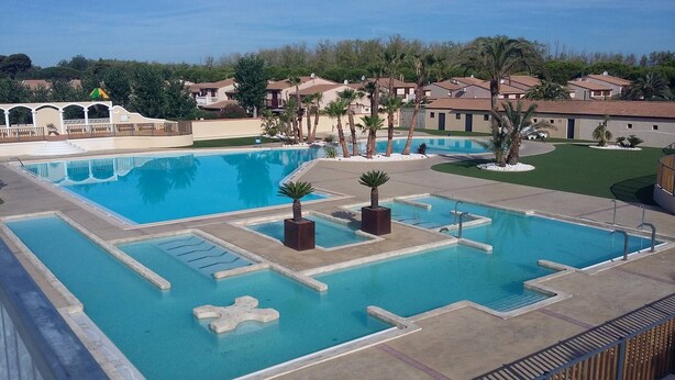 A large swimming pool with multiple lanes, surrounded by palm trees and a view of residential buildings. - Nice corner villa located with airco in LES TAMARIS (pool extra fees), 2 bedrooms, 3 stars, Wifi,... (PORTIRAGNES)