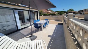 An outdoor patio with a table and chairs, a large umbrella, and a view of a building with a tiled roof. - Nice corner villa located with airco in LES TAMARIS (pool extra fees), 2 bedrooms, 3 stars, Wifi,... (PORTIRAGNES)