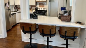 Une cuisine moderne dotée d’un îlot central, de tabourets de bar en bois et d’appareils électroménagers en acier inoxydable.