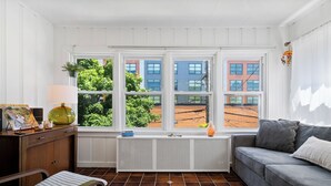 Une pièce dotée d’une grande fenêtre, d’un radiateur, d’un canapé, d’un banc et d’une petite table sur laquelle se trouvent une lampe et des objets décoratifs.