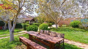 An outdoor wooden picnic table with benches, surrounded by lush greenery and trees.