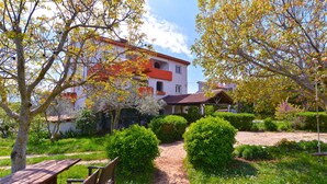 A garden path leading to a building with a red roof and white walls, surrounded by lush greenery and trees with autumn leaves.