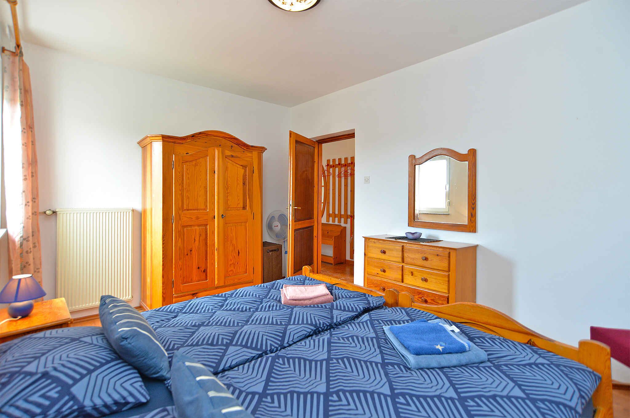 A bedroom with a bed, wooden wardrobe, dresser, and a mirror.