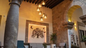 A lobby with stone columns, a wooden ceiling, a seating area with sofas and chairs, and a wall-mounted tree decoration. - Hotel Don Carlos (Morelia)