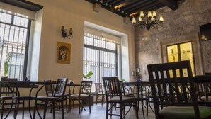 A dining area with wooden chairs and tables, large windows with metal bars, and a chandelier. - Hotel Don Carlos (Morelia)