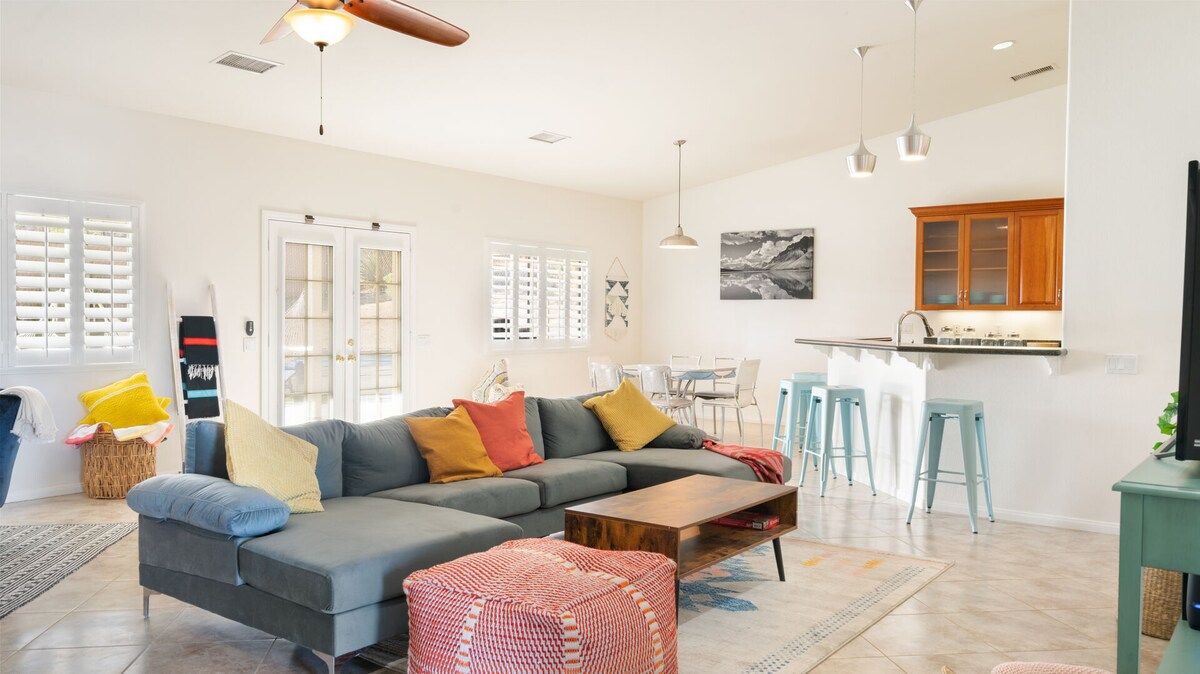 A modern living room with a sectional sofa, a coffee table, and a dining area with a kitchen in the background.
