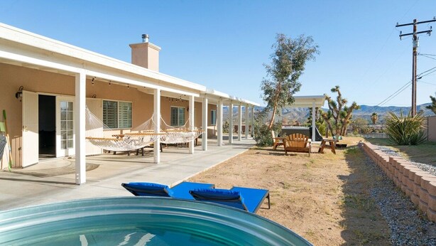 Un área de piscina con sillones de descanso, una hamaca y un porche cubierto.