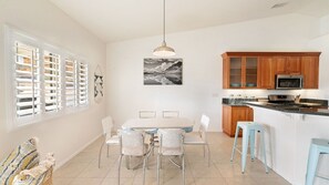 A modern kitchen with wooden cabinets, a dining table with chairs, and a hanging pendant light. - Hillside Desert House - Hot Tub, Fire Pit and BBQ (Yucca Valley)