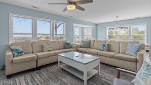 A living room with a sectional sofa, a glass coffee table, and a ceiling fan. - Shore Thing West -Spacious Beachfront Oasis & Pool - 5BR (Emerald Isle)