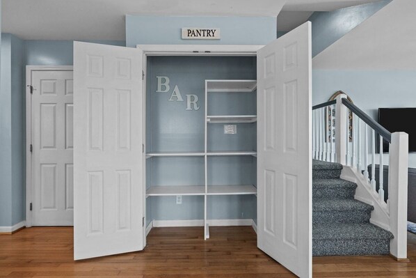 A corner pantry with open doors, a staircase, and a 'PANTRY' sign above. - Shore Thing West -Spacious Beachfront Oasis & Pool - 5BR (Emerald Isle)