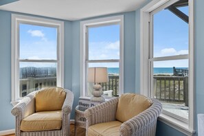 A room with two wicker chairs, a lamp, and large windows with a view of the beach. - Shore Thing West -Spacious Beachfront Oasis & Pool - 5BR (Emerald Isle)
