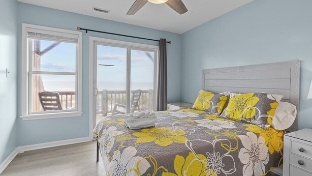 A bedroom with a bed, a nightstand, a ceiling fan, and a view of the outdoors. - Shore Thing West -Spacious Beachfront Oasis & Pool - 5BR (Emerald Isle)