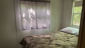 A bedroom with a bed, a window with a checkered curtain, and a view of greenery outside. - Kagawong Blue (Spring Bay)