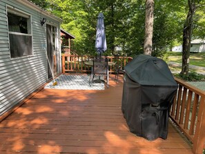 A covered outdoor grill, a patio table with chairs, and a wooden deck with a railing.