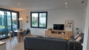 Un salon moderne avec un canapé, un téléviseur et un coin repas comprenant des chaises et une table.