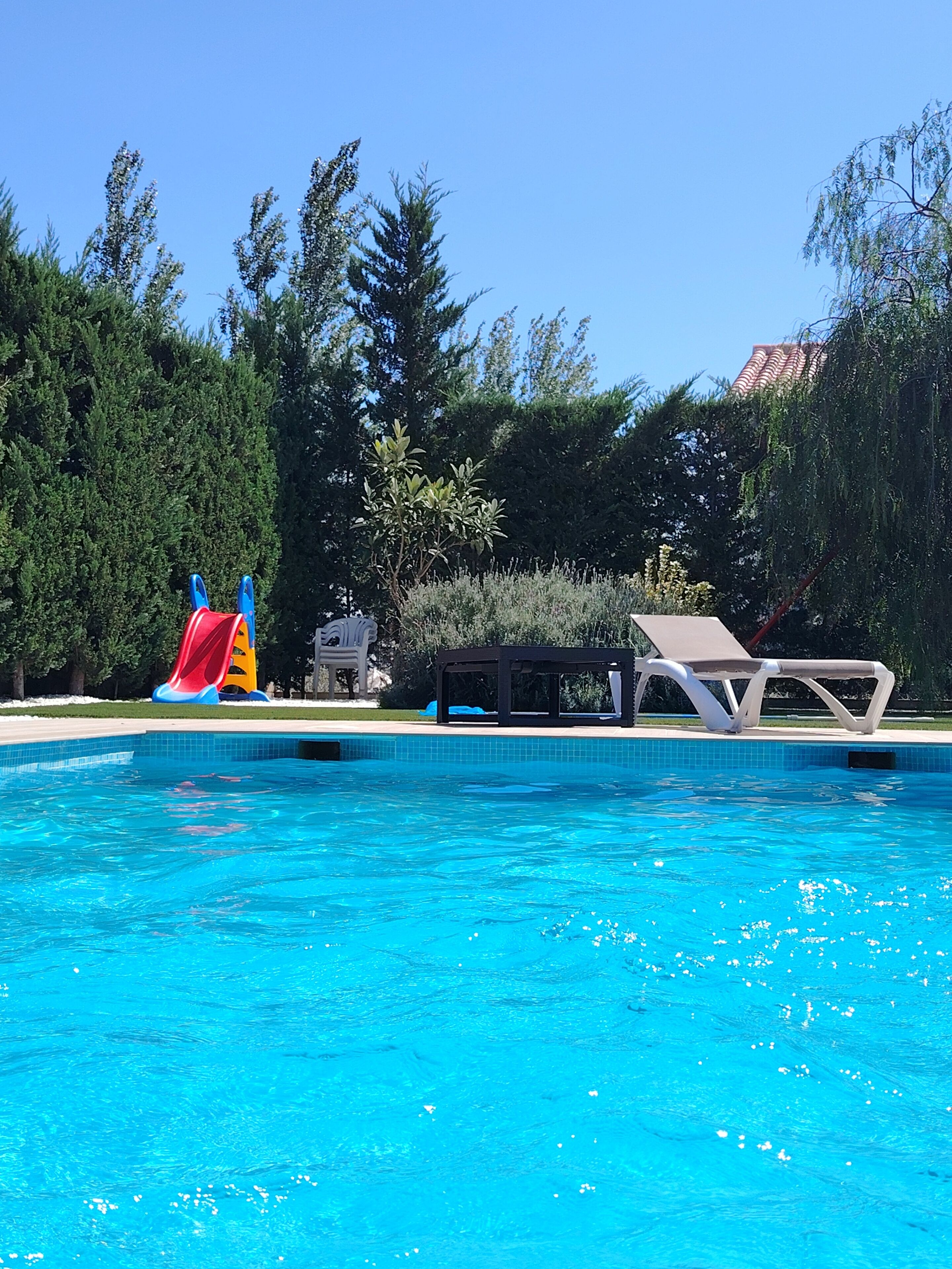 Ein Schwimmbad mit Rutsche, Liegestühlen und einer Pergola.