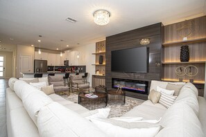 A modern living room with a large flat-screen TV, a fireplace, and a cozy seating area.