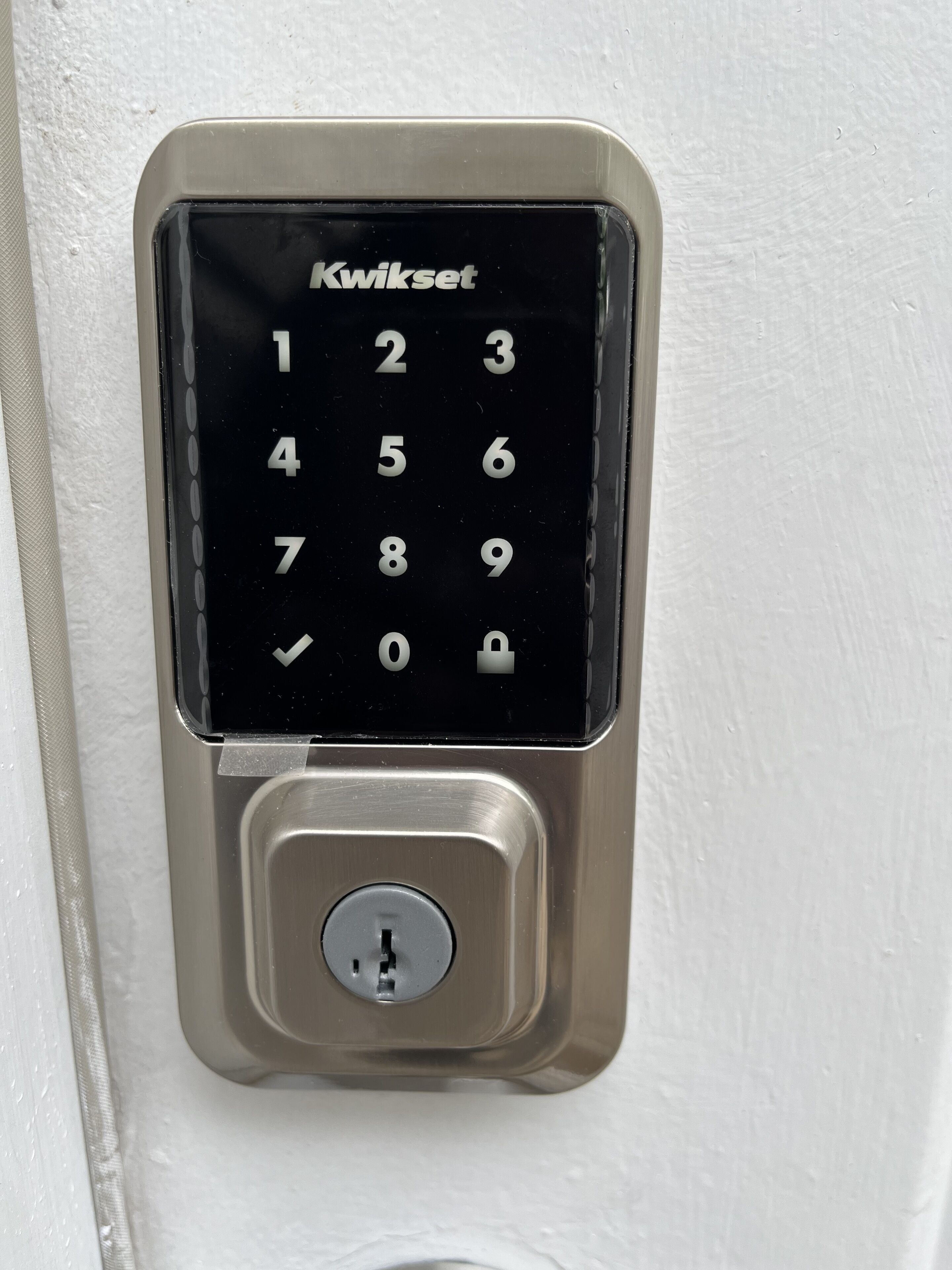Cerradura electrónica con teclado numérico Kwikset montada en una pared blanca.