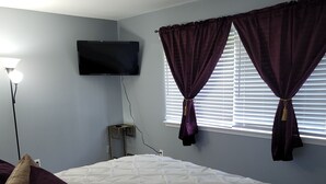 A bedroom with a large bed, a flat-screen TV mounted on the wall, and a window with curtains. - The Heart of Raleigh (Raleigh)