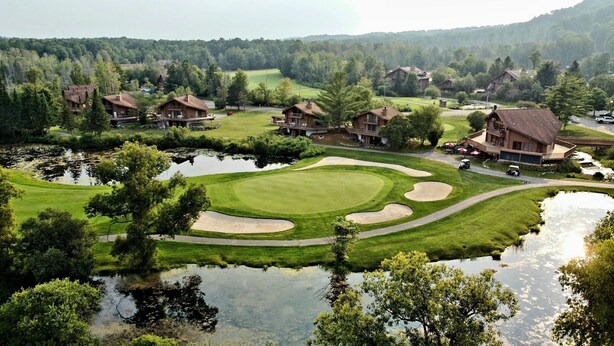 A golf course with bunkers, a pond, and surrounding houses. - Modern NEWLY renovated 1 bedrm, WIFI, Pool, new kitchen Summer of 24!  sleeps 4. (Mancelona)