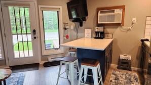 A kitchen with a bar area, a coffee machine, and a TV mounted above the counter. - Modern NEWLY renovated 1 bedrm, WIFI, Pool, new kitchen Summer of 24!  sleeps 4. (Mancelona)