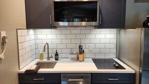 A modern kitchen with dark cabinets, a stainless steel microwave, a double sink, and a dishwasher. - Modern NEWLY renovated 1 bedrm, WIFI, Pool, new kitchen Summer of 24!  sleeps 4. (Mancelona)