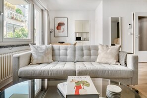 Ein modernes Wohnzimmer mit einem grauen Sofa, einem Glastisch und einem Buch mit dem Titel 'The Infolk Garden'.
