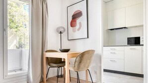 A modern kitchen with white cabinets, a black microwave, and a wooden dining table with two chairs. - Premium Iselin 1 Room w/ Storage, 1min to Local Market, by Blueground (Basel)