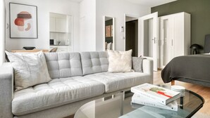 A modern living room with a grey sofa, a glass coffee table, and a bookshelf. - Premium Iselin 1 Room w/ Storage, 1min to Local Market, by Blueground (Basel)