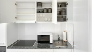 A modern kitchen with a built-in microwave, a stainless steel sink, and open cabinets containing kitchenware. - Premium Iselin 1 Room w/ Storage, 1min to Local Market, by Blueground (Basel)