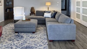 Una sala de estar con un sofá modular, un sillón blanco, una mesita auxiliar con lámpara y un jarrón decorativo.