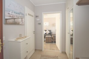 Corredor que dá para um quarto com cama, cômoda e um quadro de gaivotas.