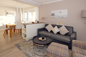 Uma sala de estar moderna com um sofá cinzento, uma mesa de centro redonda e um espaço de jantar com mesa e cadeiras de madeira.