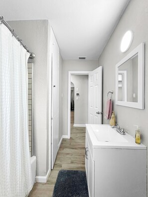 A bathroom with a white sink, a mirror, and a shower curtain. - The Pink Pearl (St. Petersburg)