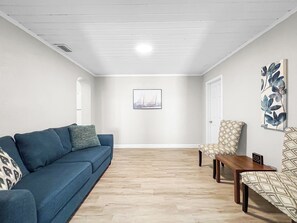 Una habitación con un sofá azul, un sillón estampado, una mesa de madera y un cuadro en la pared.