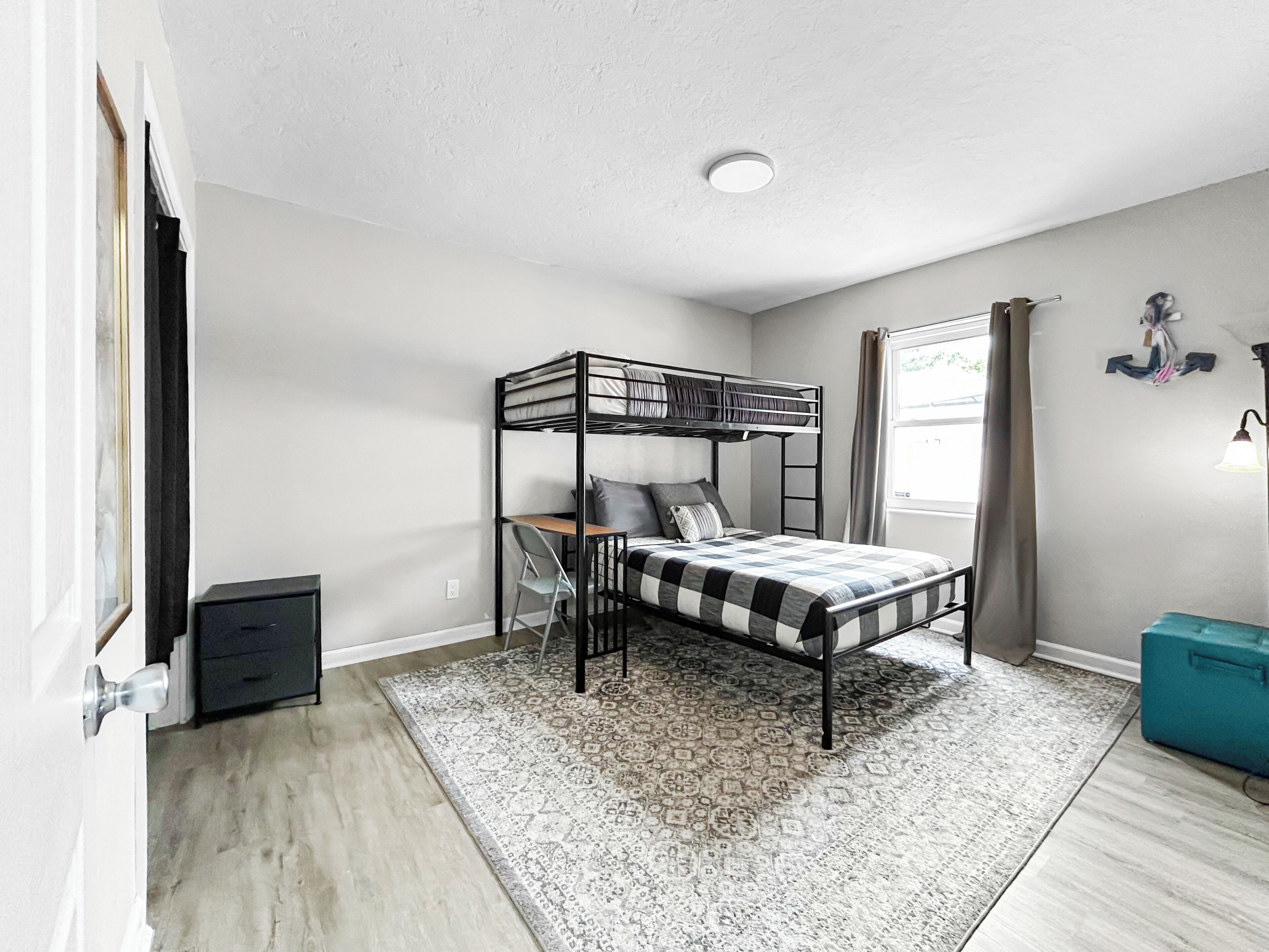 A bunk bed room with a desk, a patterned rug, and a small storage box.