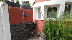 A small outdoor shower area with a stone wall, a red and black wall, and a window. - Vacation home 5 minutes from the beach (Agde)