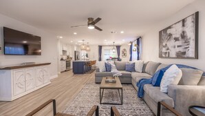 A modern living room with a sofa, coffee table, and a TV. There is a kitchen area with cabinets and a dining table. - Gem in Heart of Old Town Scottsdale  (Scottsdale)