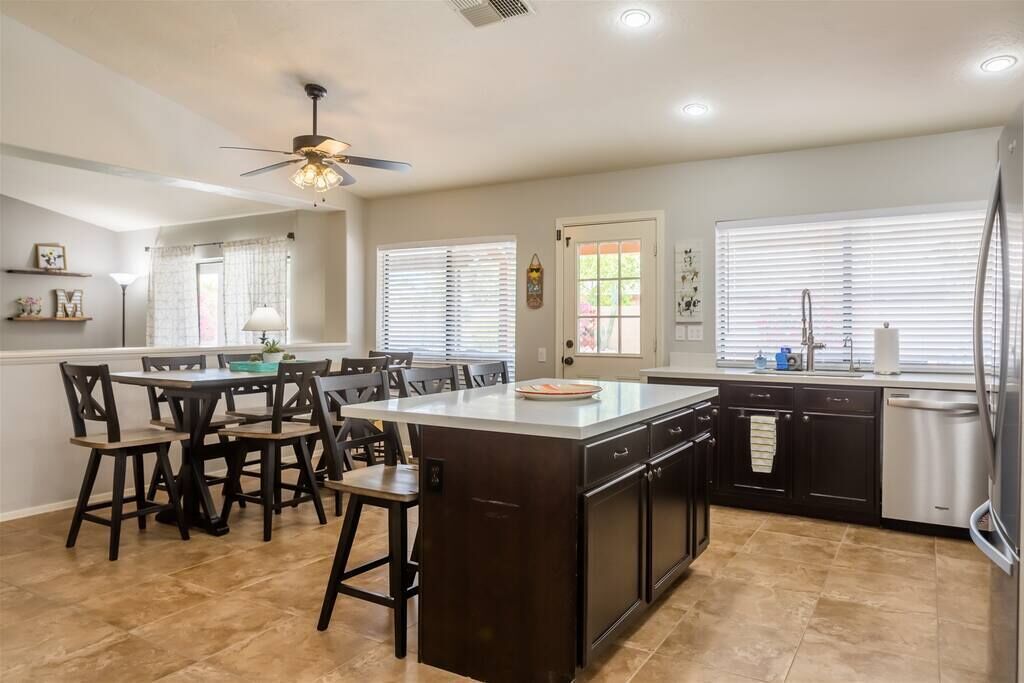 A modern kitchen with a central island, dark cabinetry, and a ceiling fan.