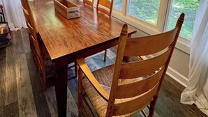Uma sala de jantar com mesa e cadeiras de madeira, janelas grandes com cortinas e um lustre.